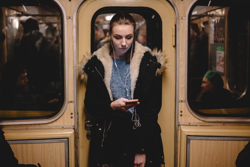 Young woman standing on a tube carriage listening to music but looking gloomy.