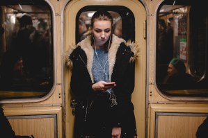 Young woman standing on a tube carriage listening to music but looking gloomy.