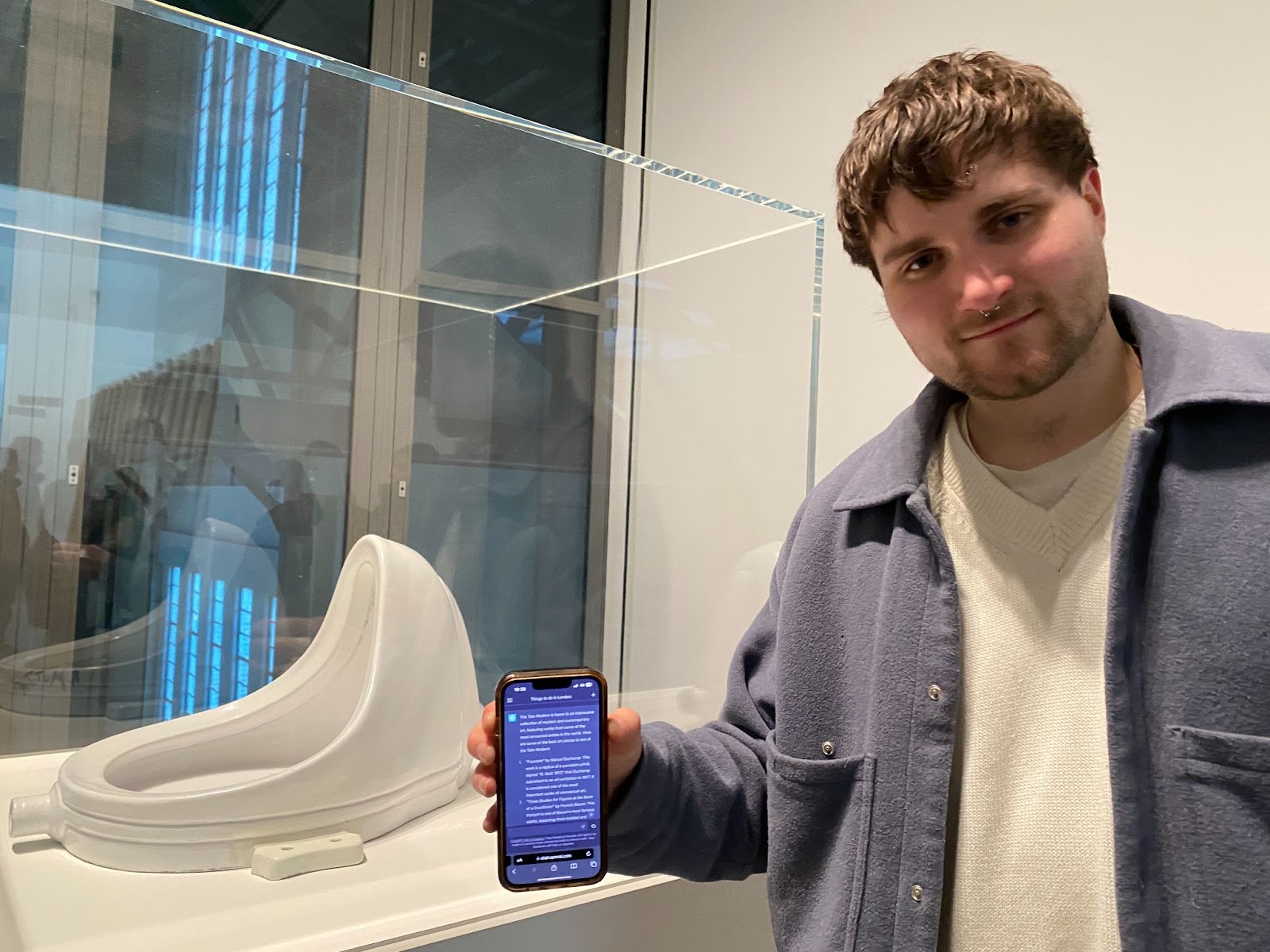 A man holding up ChatGPT on his phone next to Duchamp's Fountain