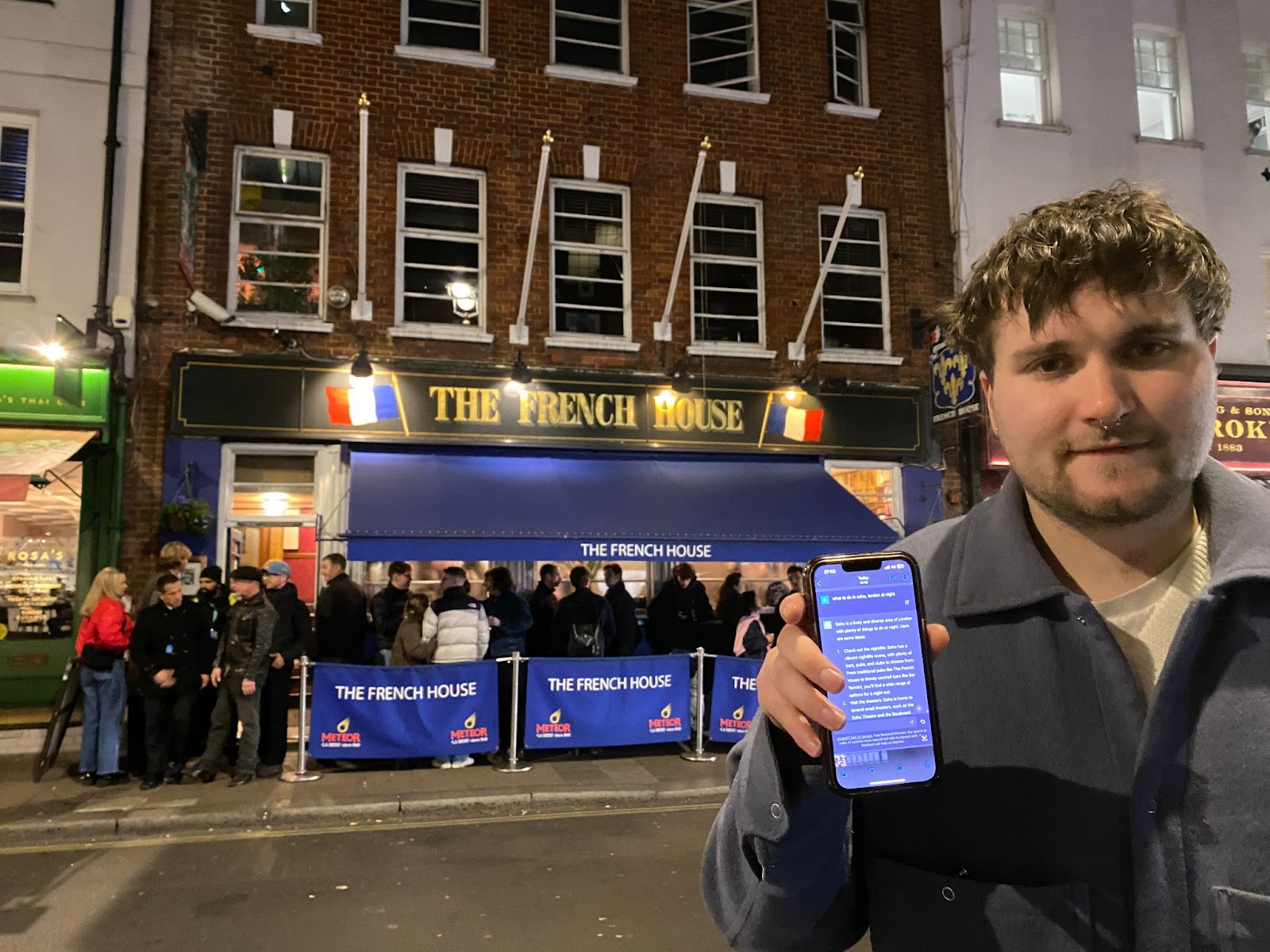 A man holding up ChatGPT on his phone outside the French House in Soho