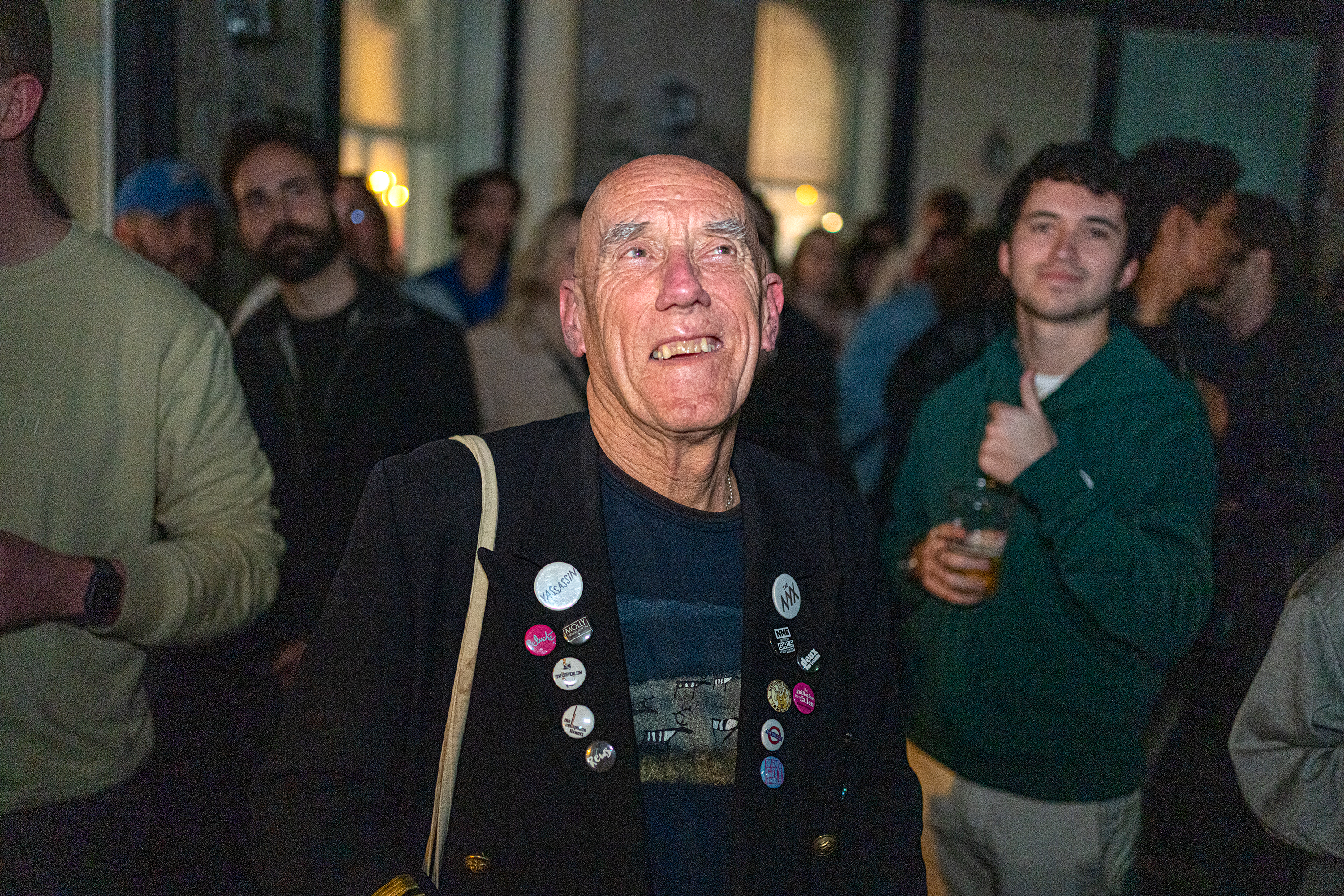 Roger looks up with a smile on his face while standing in a crowd at a music venue.
