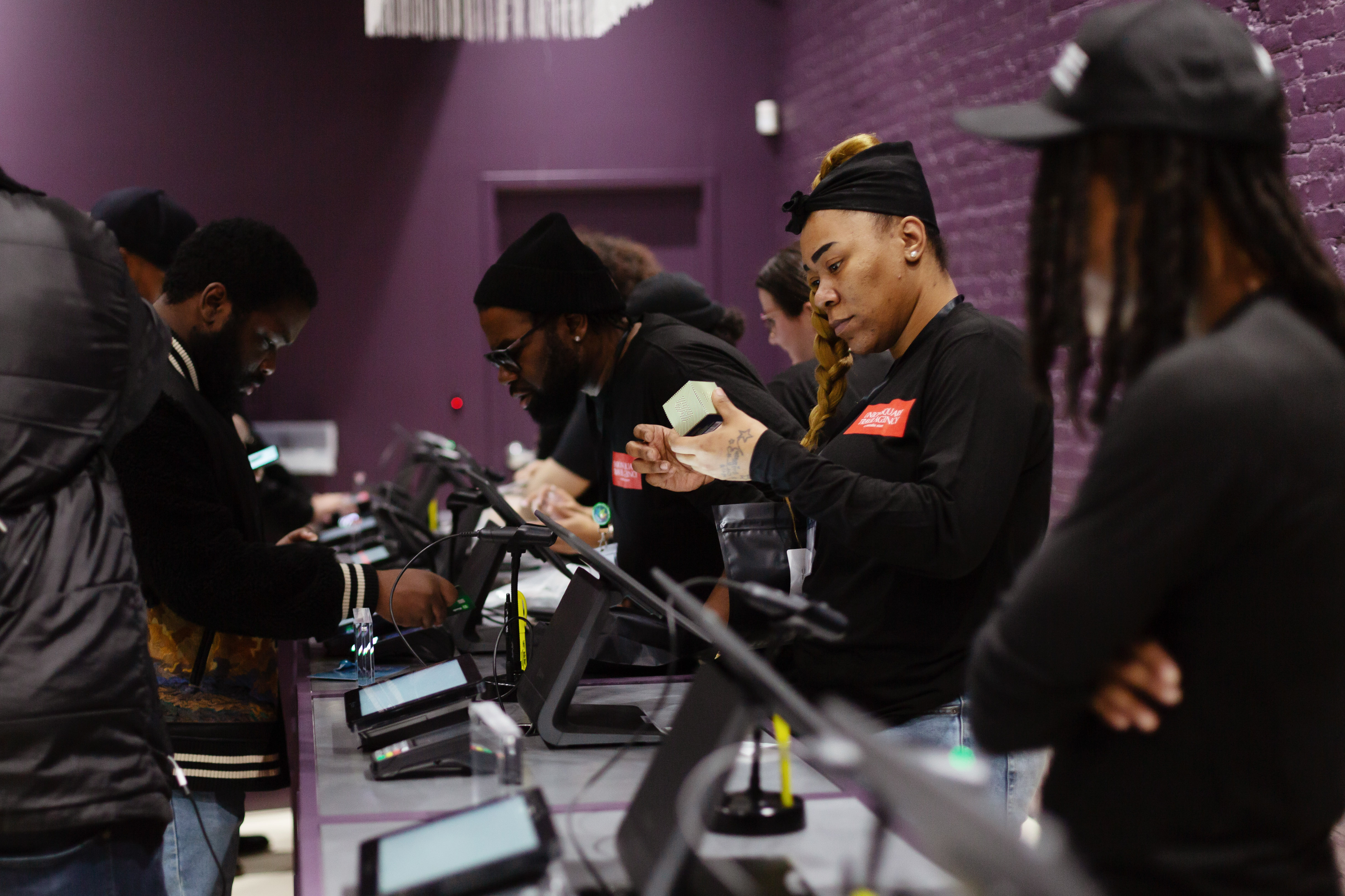 A line of budtenders check out customers in a purple walled room.