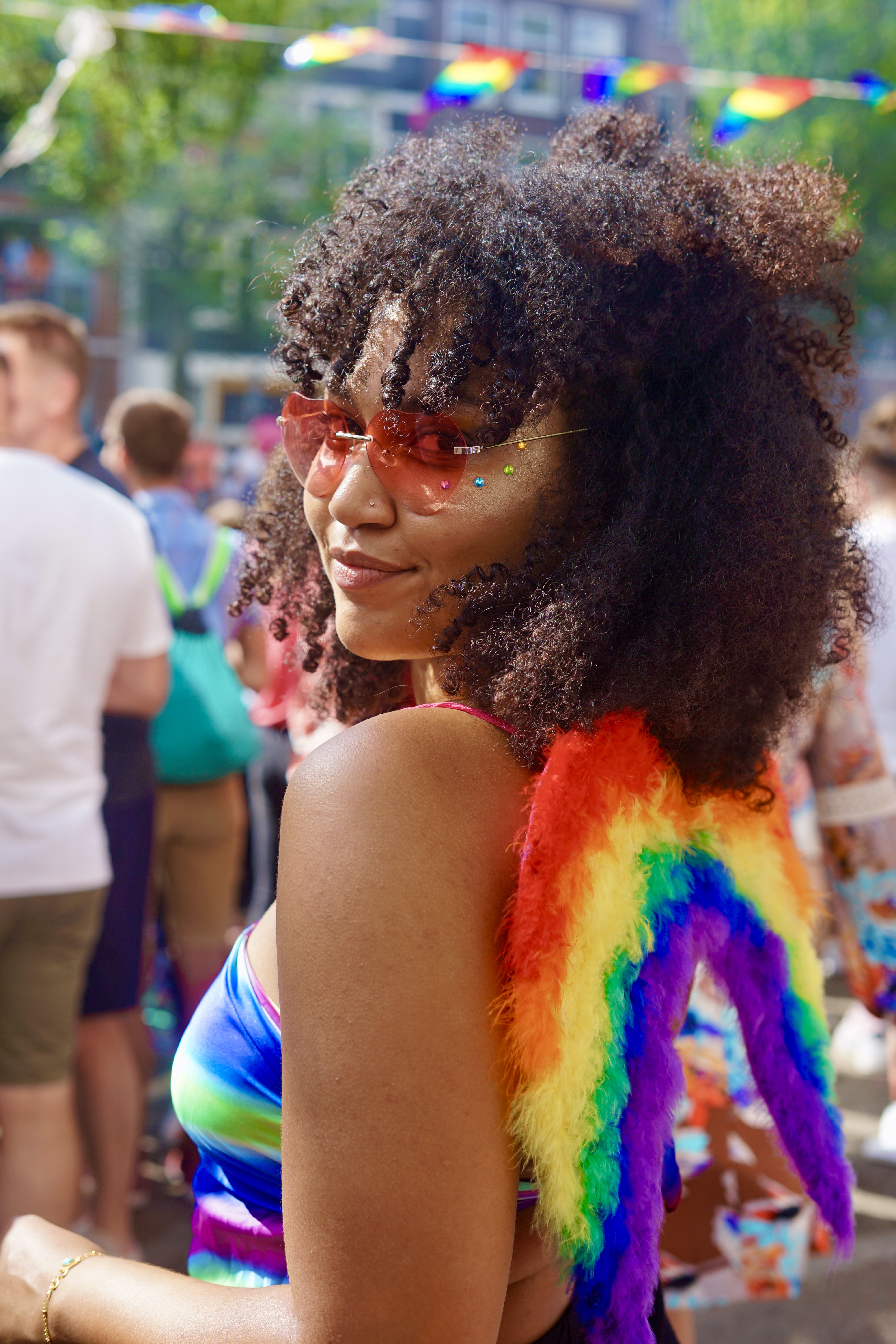 Eine Schwarze Frau in Regenbogenoutfit und mit bunter Brille schaut über die Schulter in die Kamera