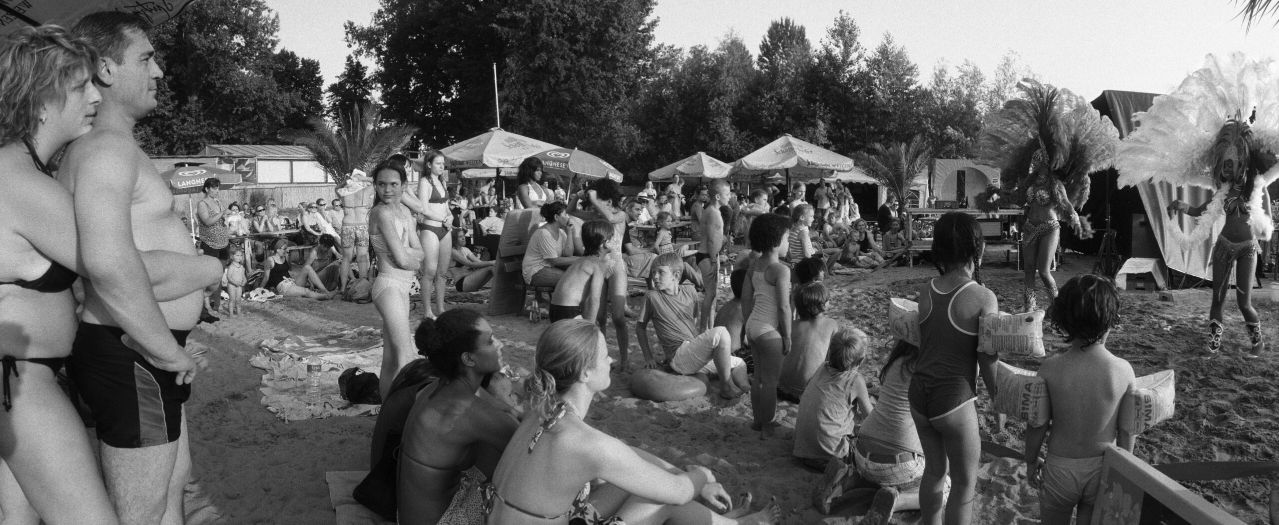 Viele Besucher in Badebekleidung beobachten den Auftritt von zwei Frauen. Die Frauen tragen südamerikanische Karnevalsoutfits.