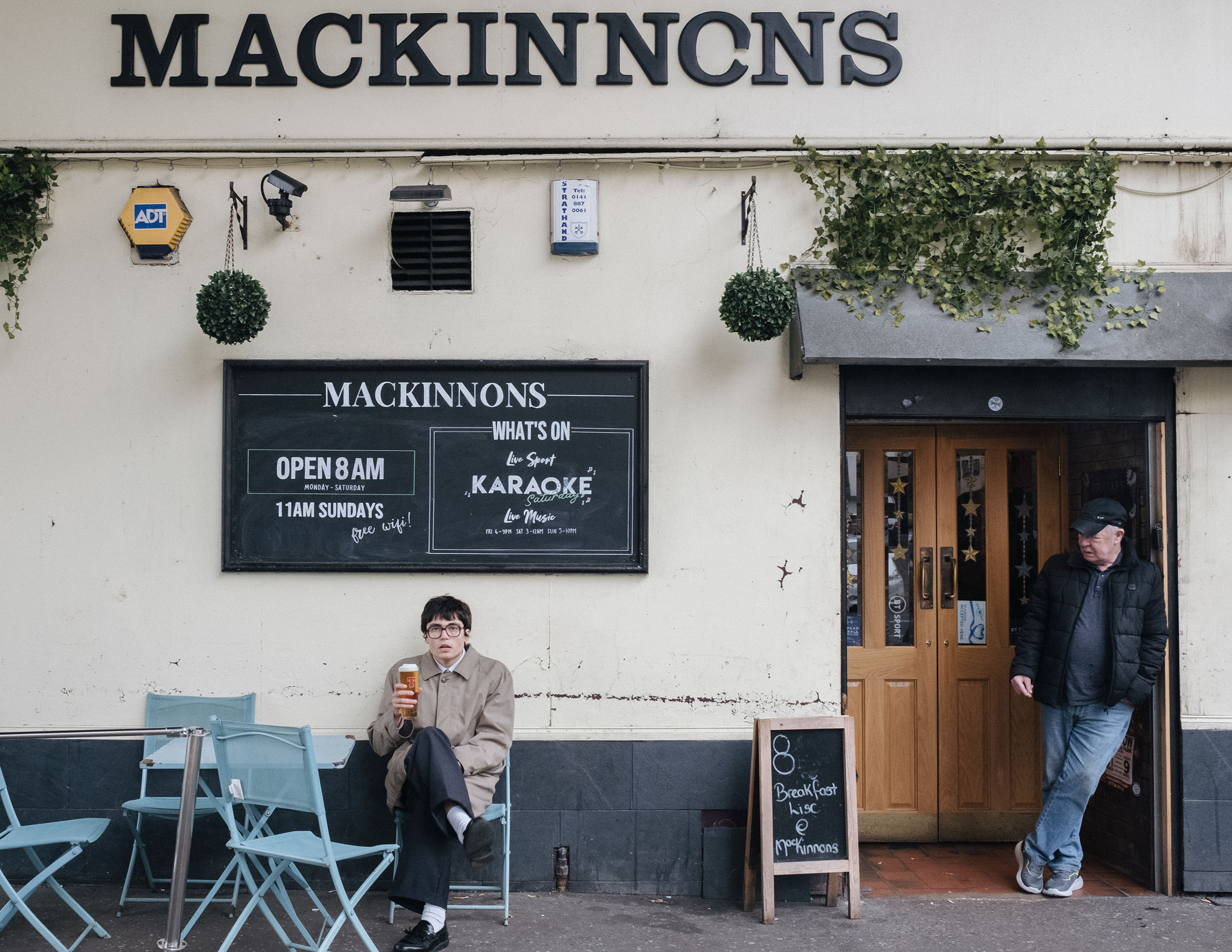 Man in glasses holding up pint outside Mackinnons in Glasgow