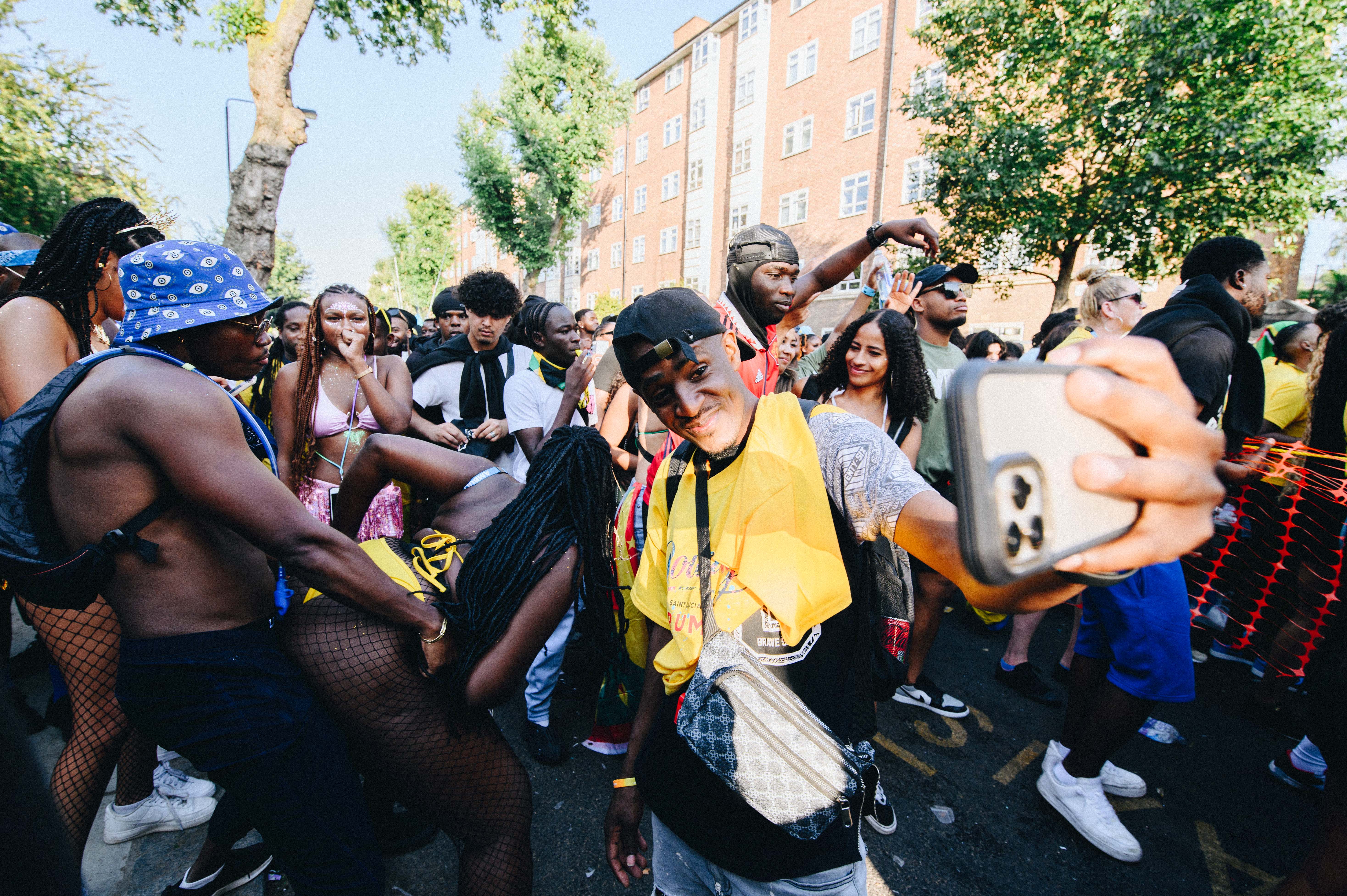 Notting Hill Carnival 2023, London: A man takes a selfie in front of a whining couple