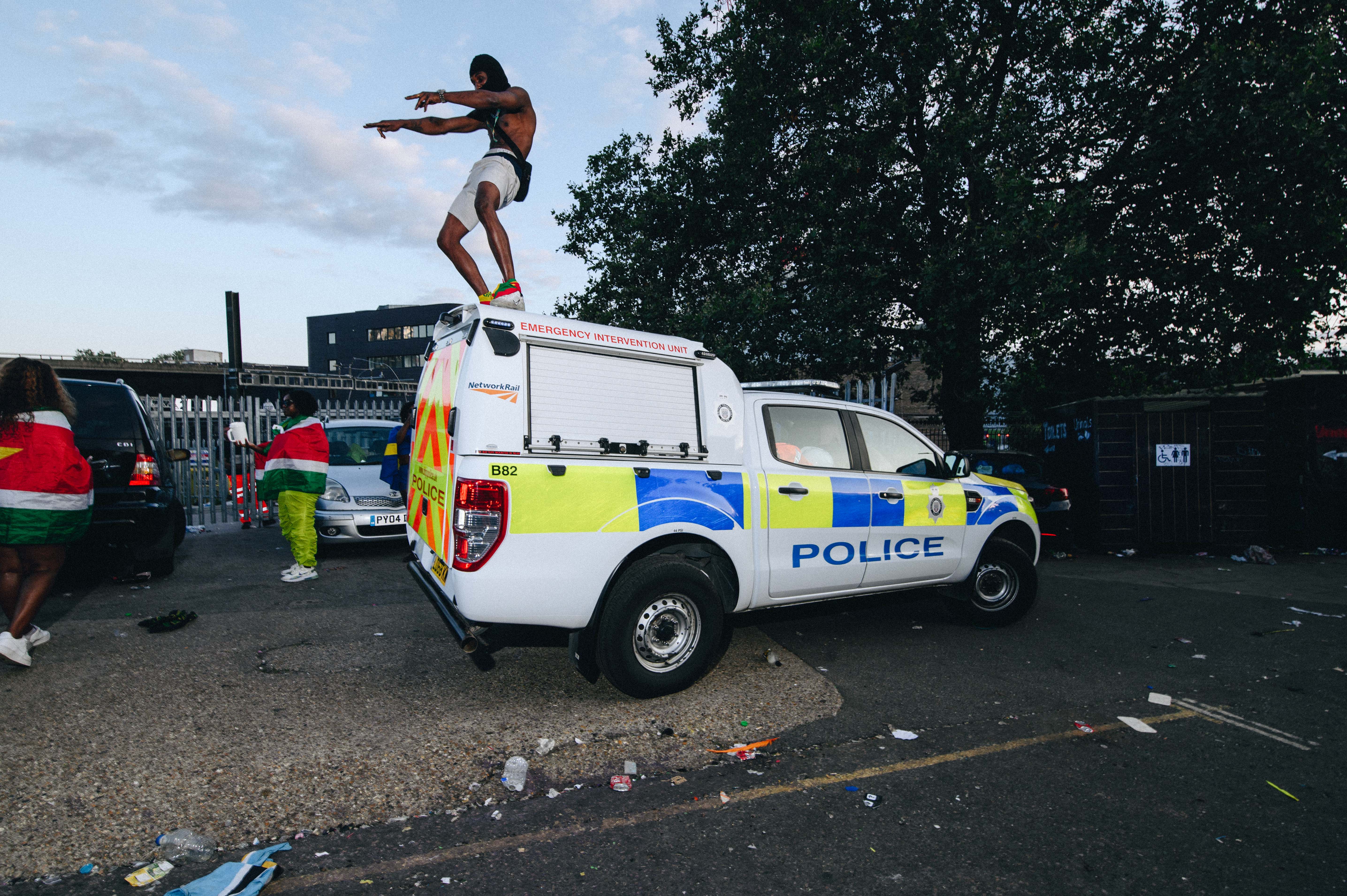 Notting Hill Carnival 2023, London: Man in a balaclava dances on top of a police car.