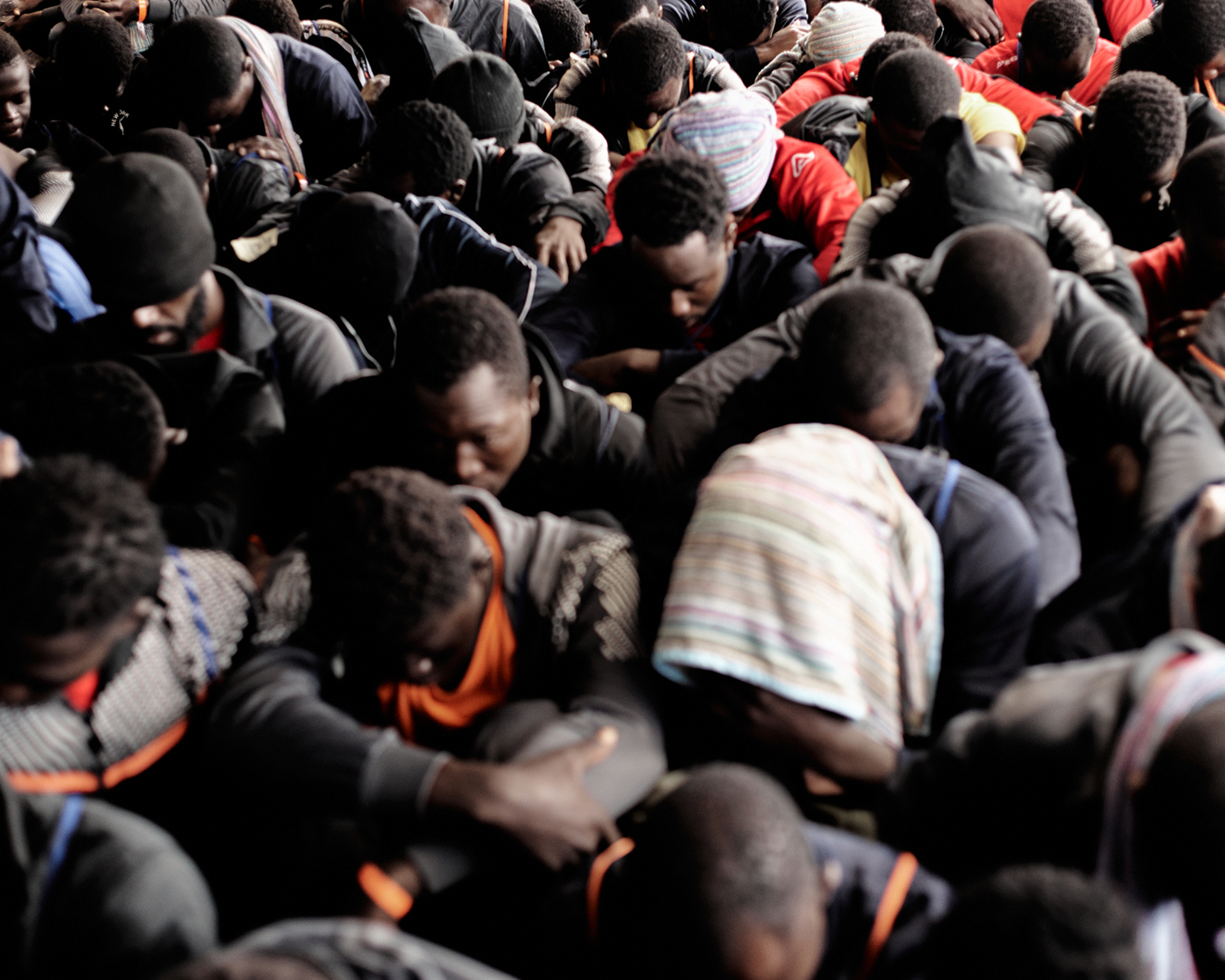 Viele Menschen sitzen voreinander auf dem Schiffsboden und richten den Blick nach unten.