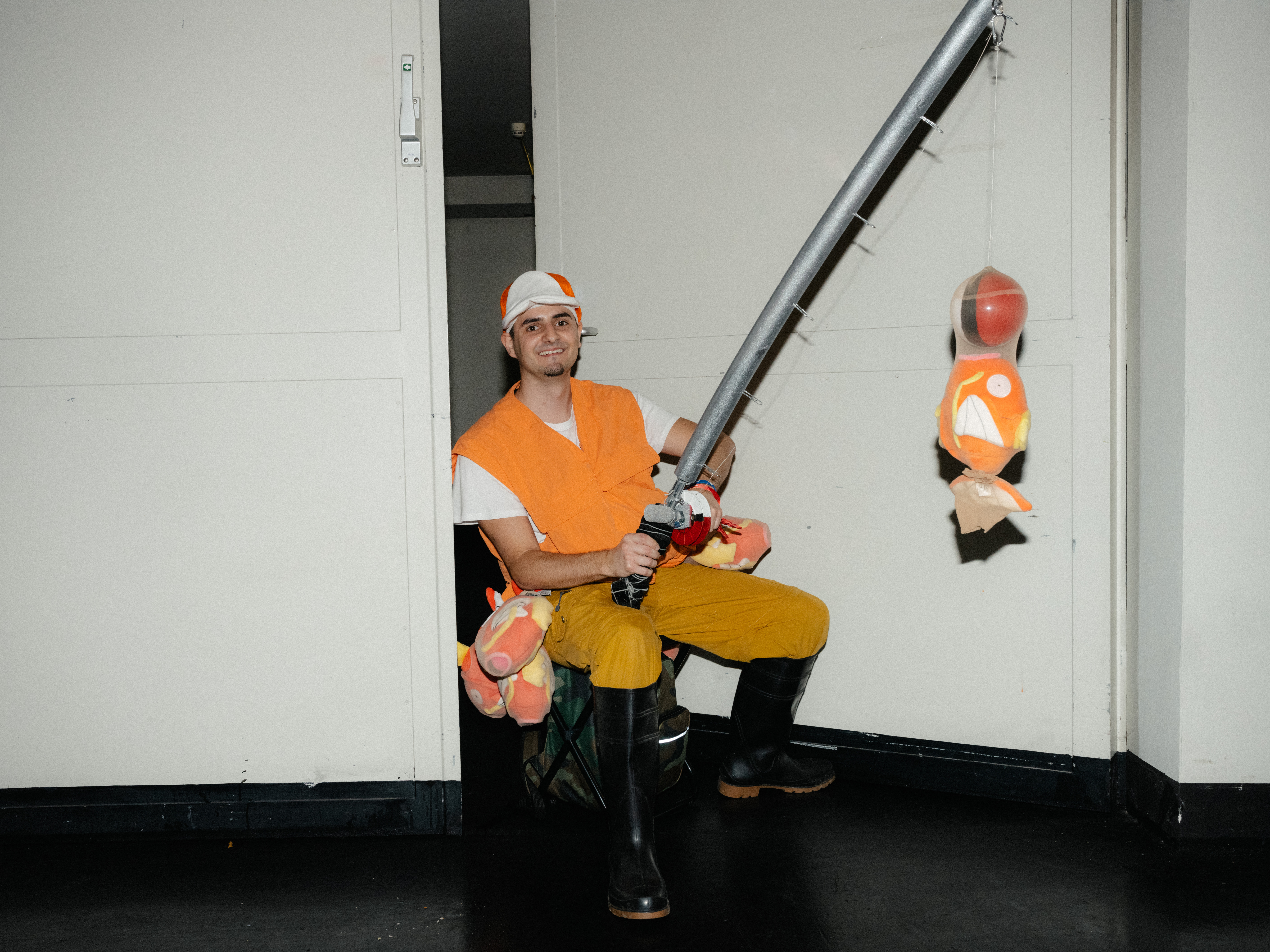 Ein Mann mit orangener Weste und einer weiß-orangenen Cap hält eine Angel mit einem Plüsch-Karpardor