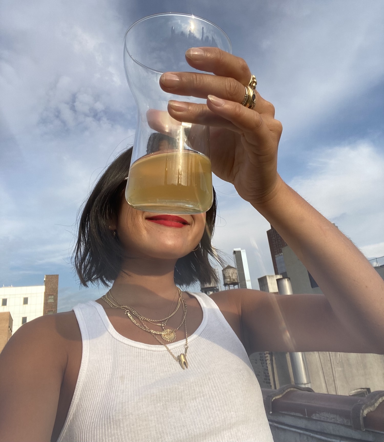 Woman in tank top holding up glass of cider wearing talisman necklace