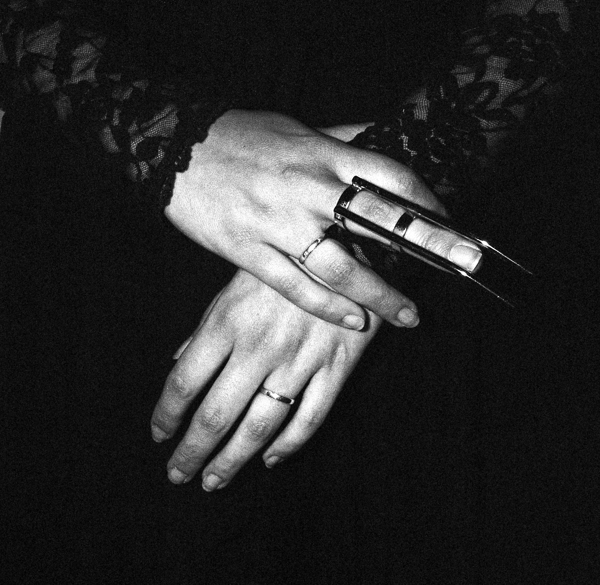 A close up of hands, right hand clasping left wrist. The person is wearing two small rings on the ring finger and a BDSM claw on the right middle finger.