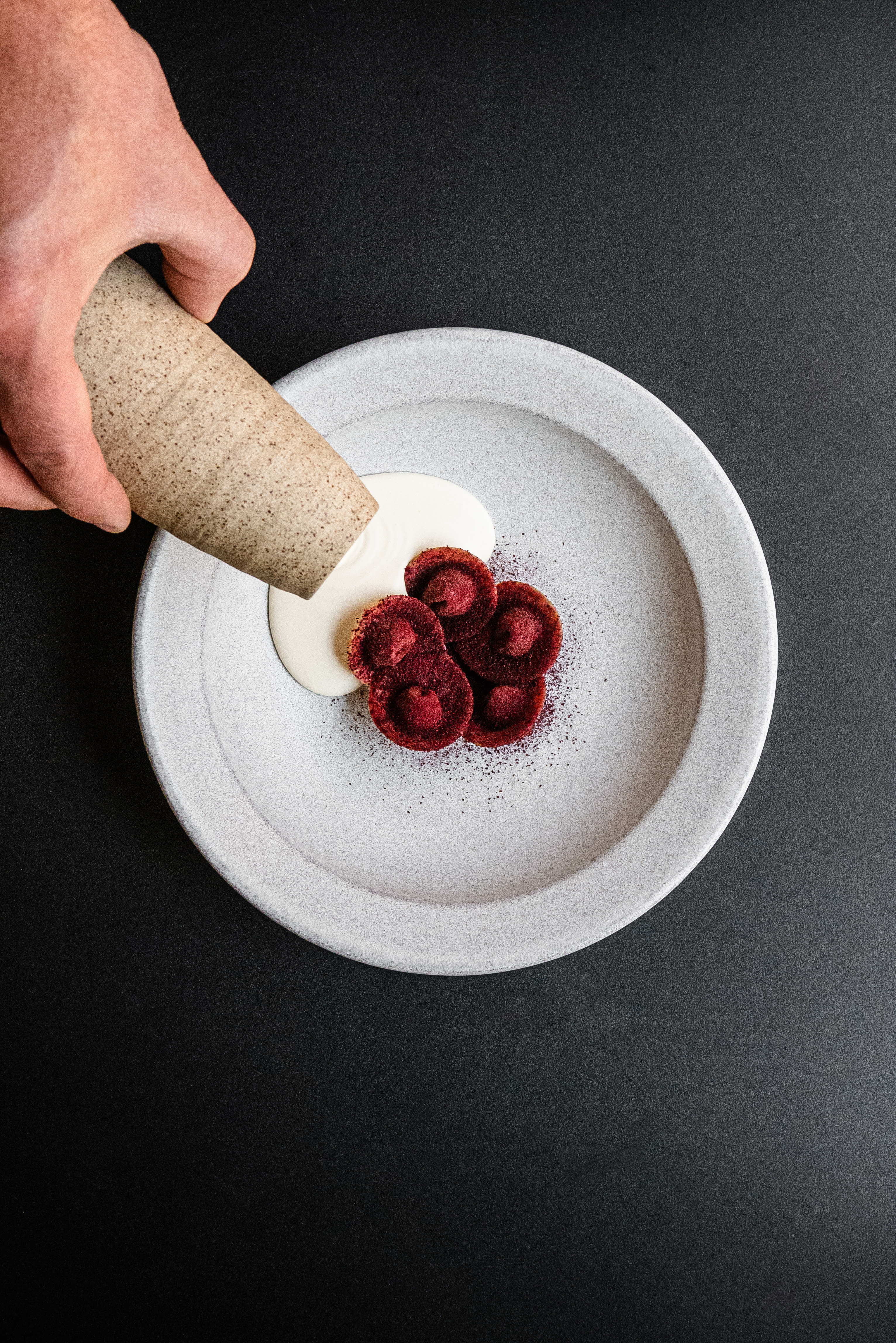 A photo of a hand pouring white cream next to a flower-shaped dessert.