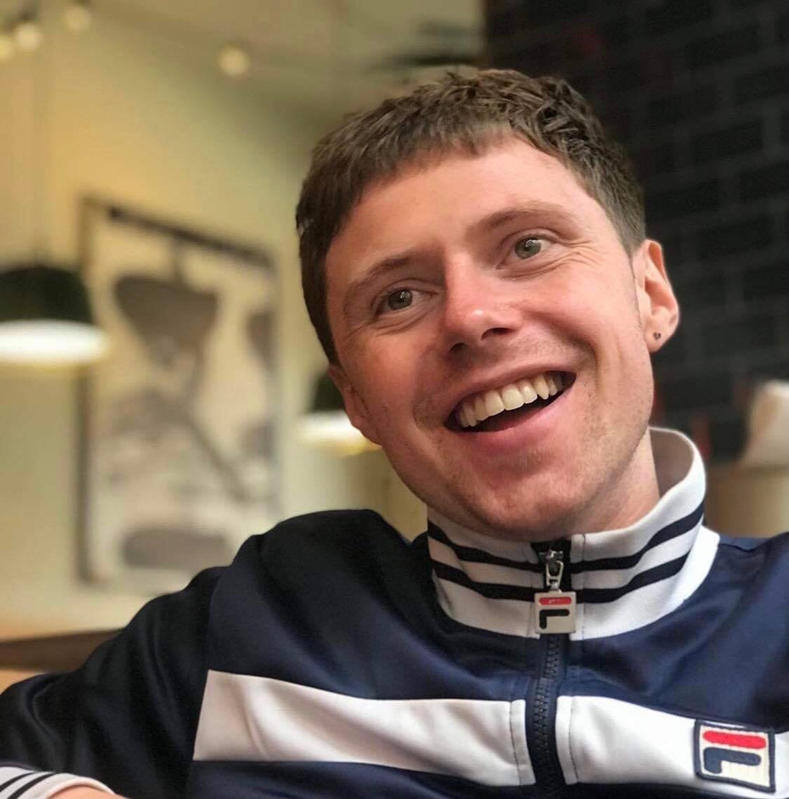 A man looks off camera and smiles, he's wearing a sports jacket zipped up to top.