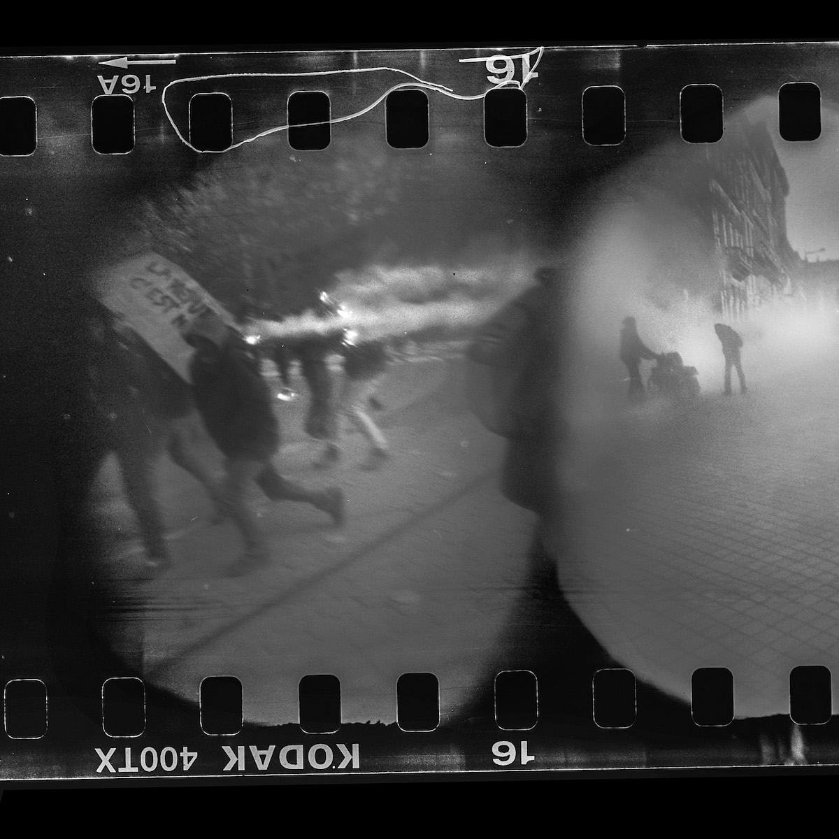 Steven Monteau photos with police weapons: black and white negative of a riot, with smoke and people running on the streets