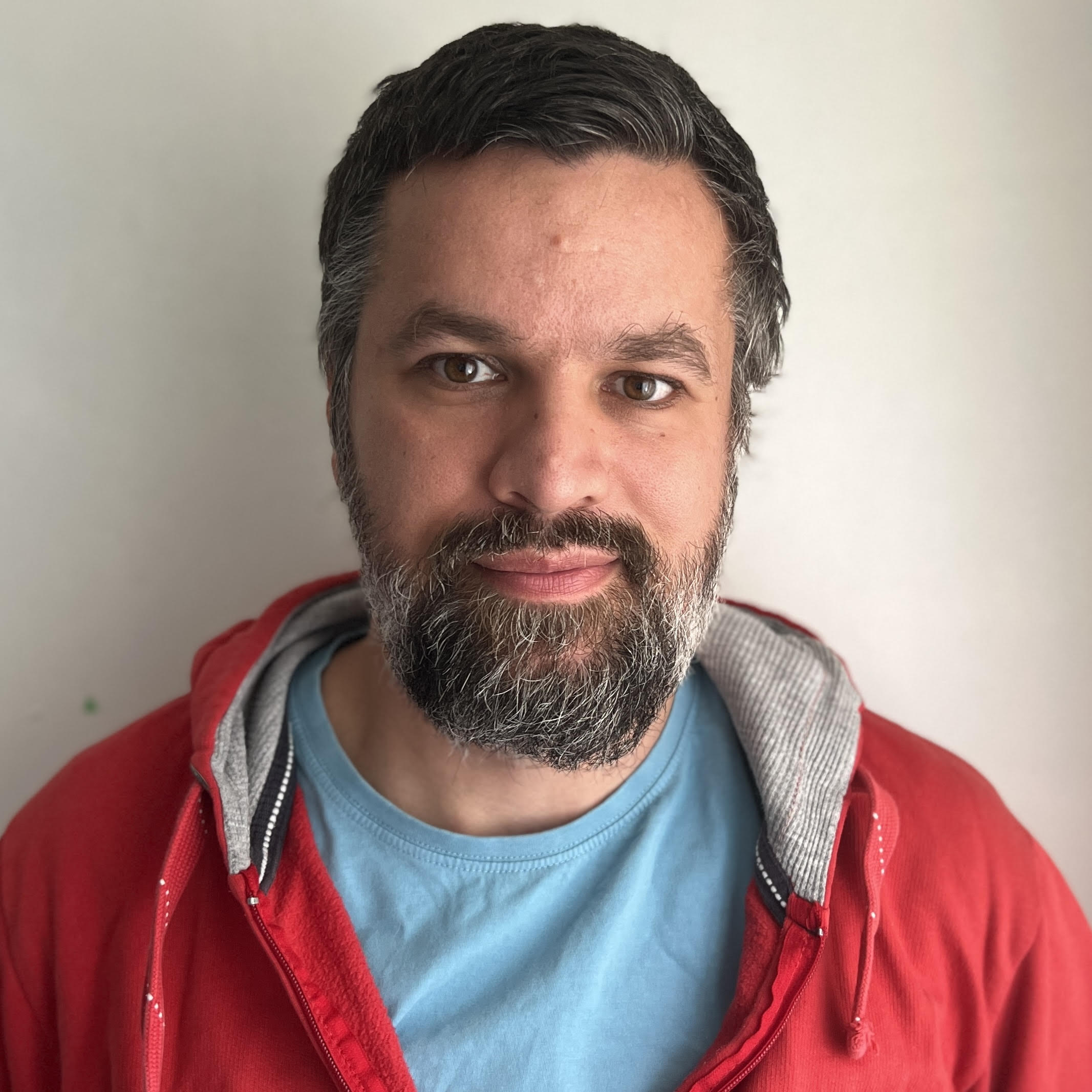 Portrait of the interview subject – he has salt and pepper hair and a beard, and is wearing a red jumper hoody.