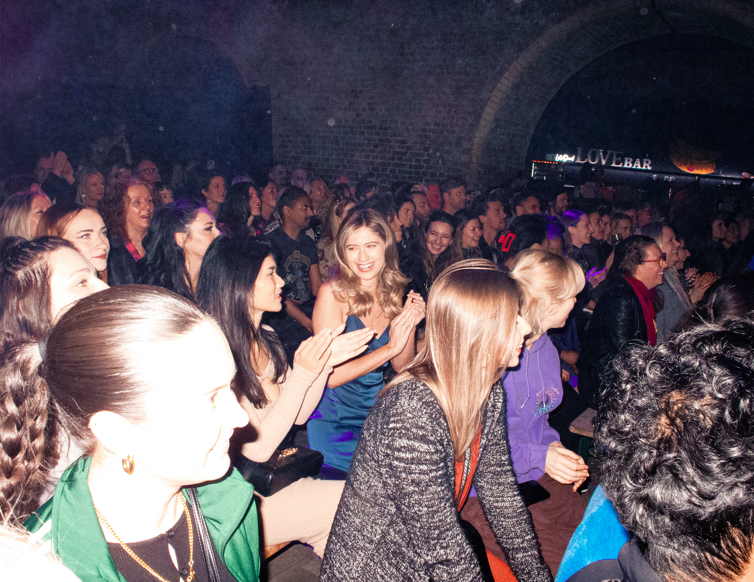 Lots of people on benches in a room, facing a stage.