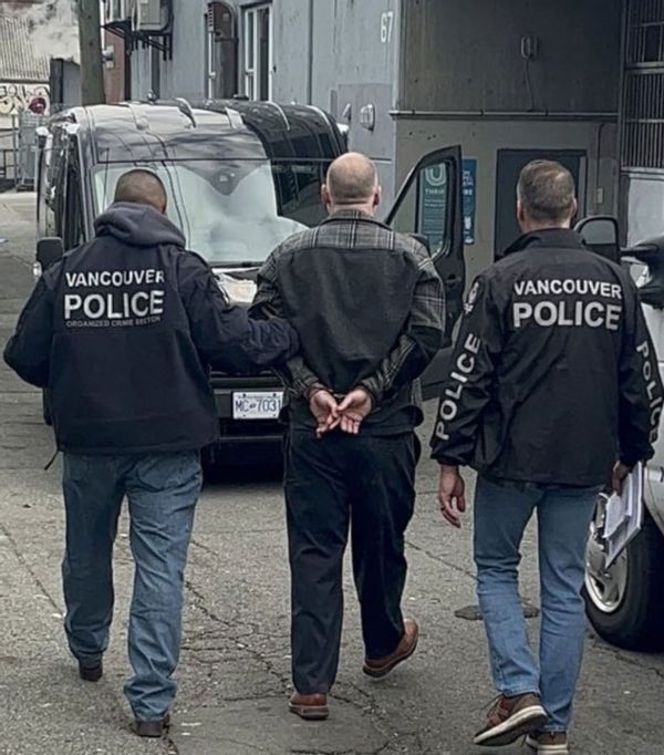 A photo of Larsen being led away by two policemen towards a black van.