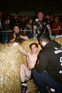 A young white boxer lies slumped against the hay bales demarcating a bare knuckle boxing ring