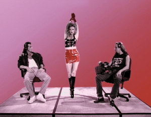 Two young men sit on office chairs while a woman in a short skirt cavorts between them