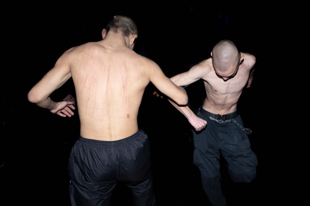 Two young people with shaven heads dance arm in arm.